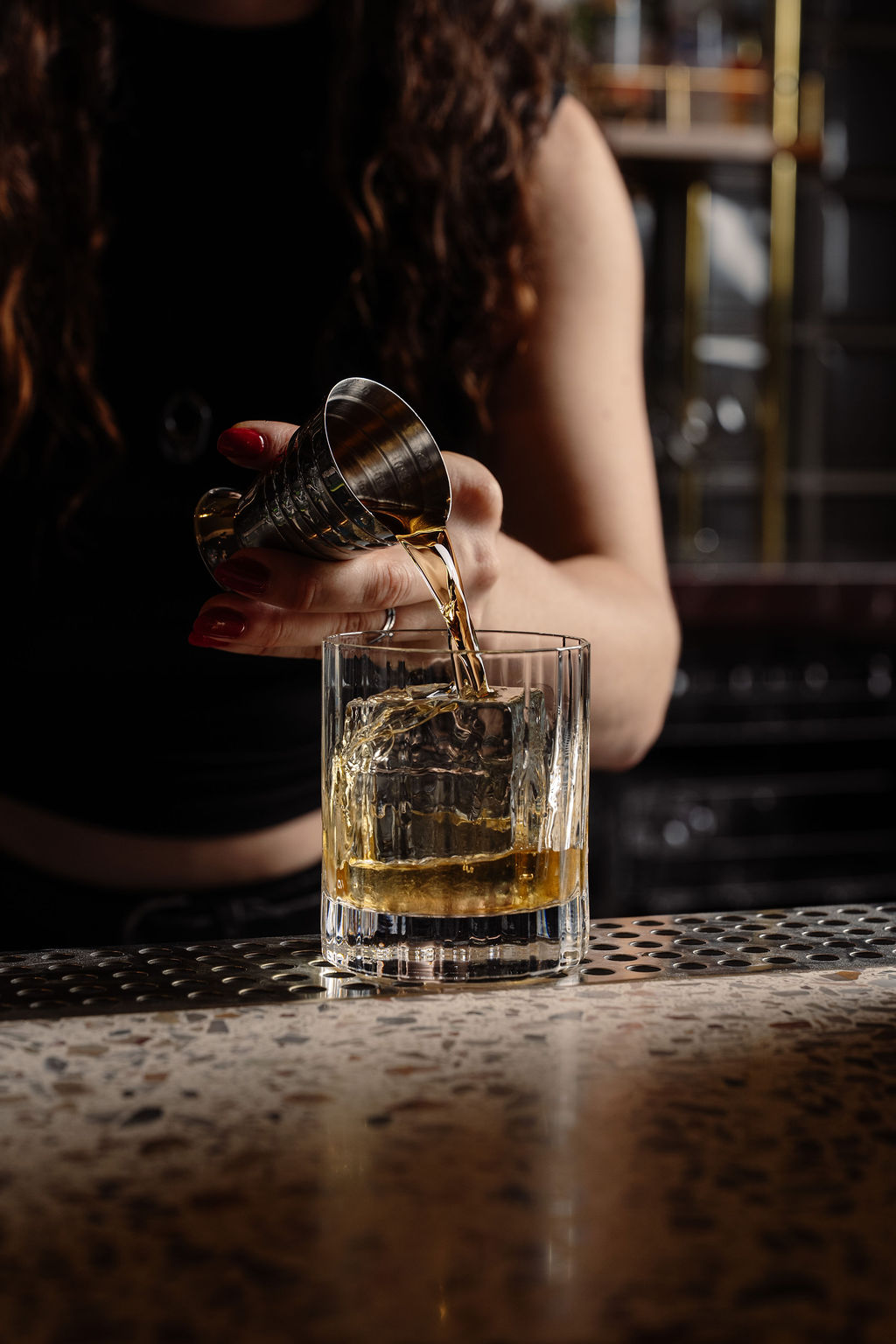 A bartender pouring amber spirit over a large ice cube at the SOHO bar